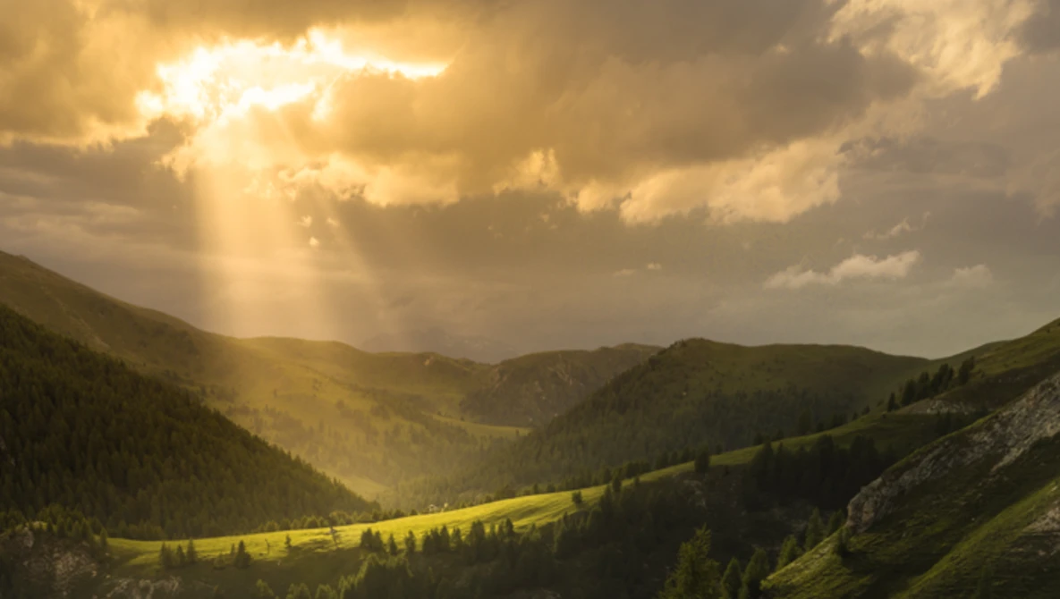 Sunlight breaking through clouds over a green mountain valley